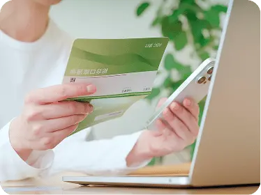 通帳を見ながらパソコンとスマホで支払いをしている女性